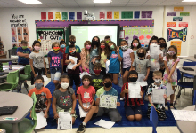 Picture of Ms. Slowik's 4th grade class. They are grouped together around a front of the classroom. A few are holding signs that say they broke out and escaped from the fun game where they learned about growth mindset and never giving up. They have masks 