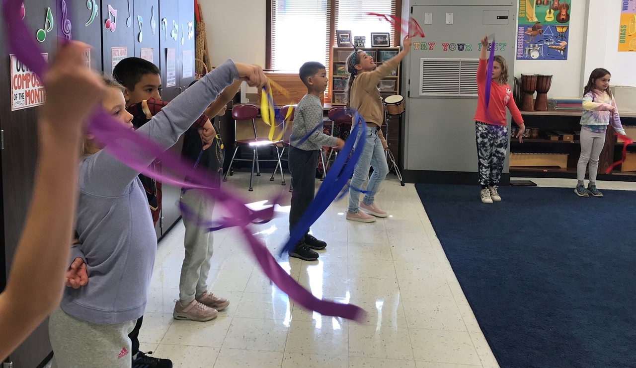 Students twirl ribbons on a wand to music during music class.