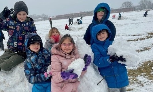 Students on the playground building a snowman during recess.