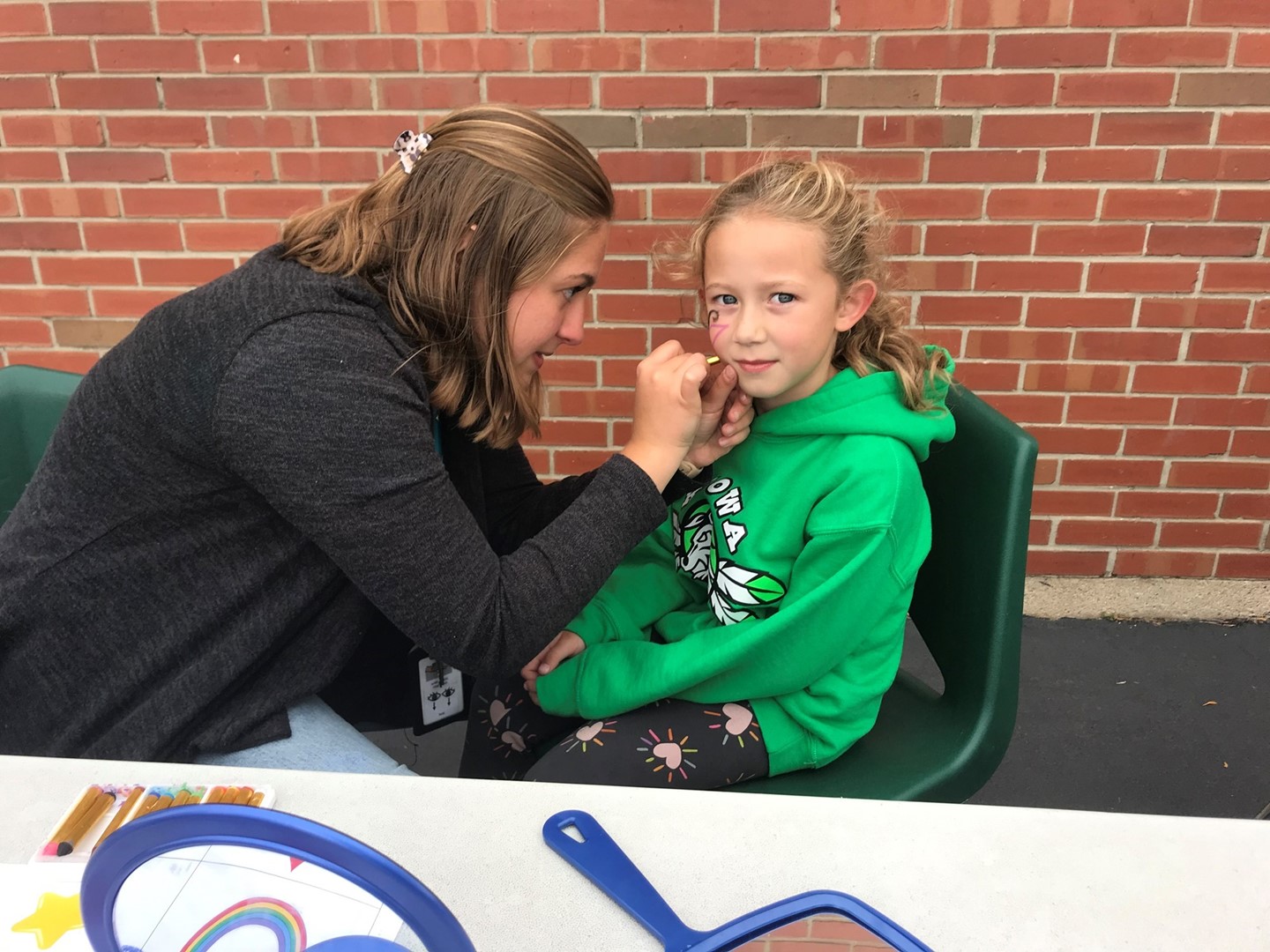 Teacher face painting a picture on a student&#39;s cheek at Family Fest Night.