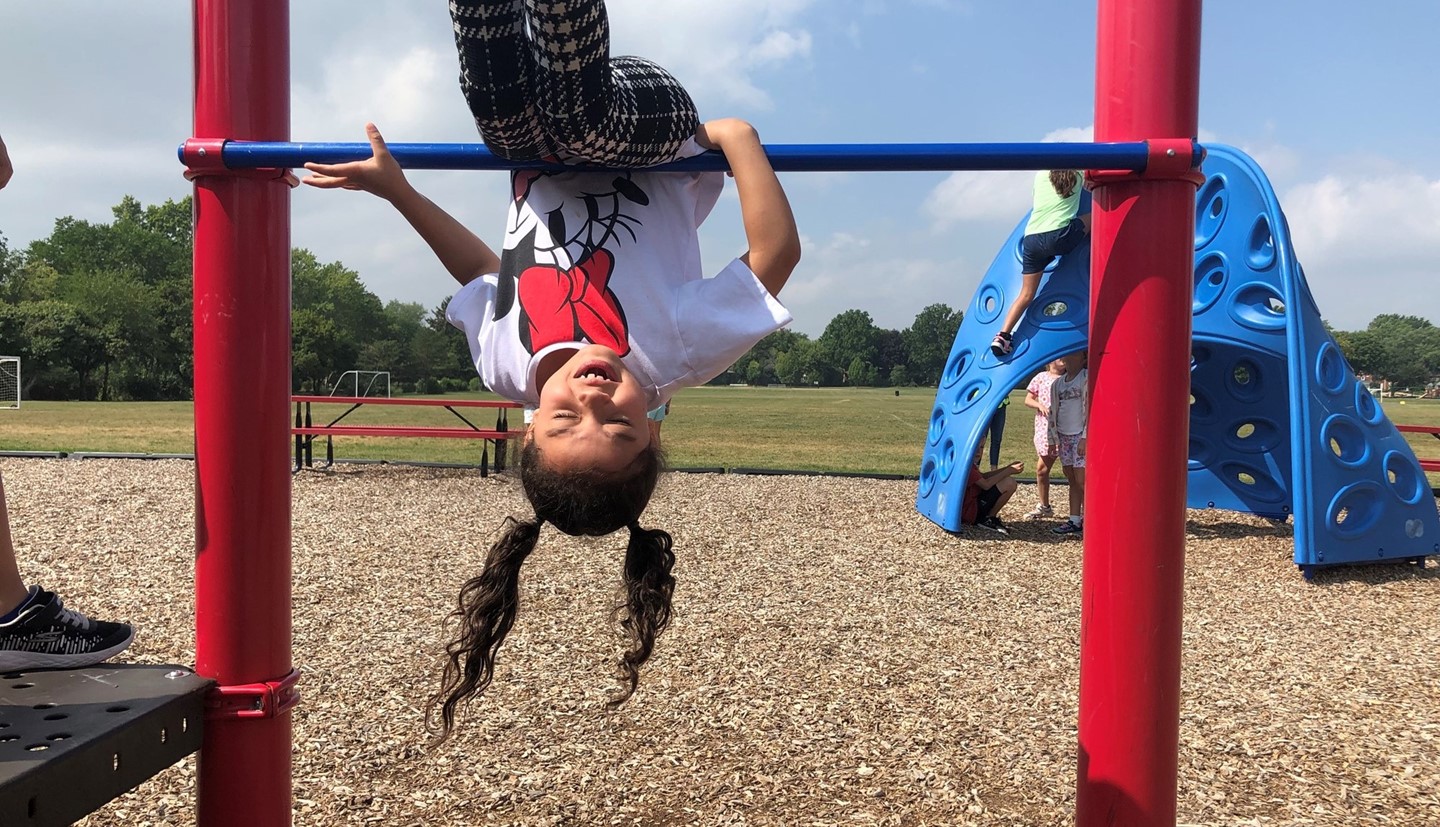 Student swinging upside down on a bar at recess.